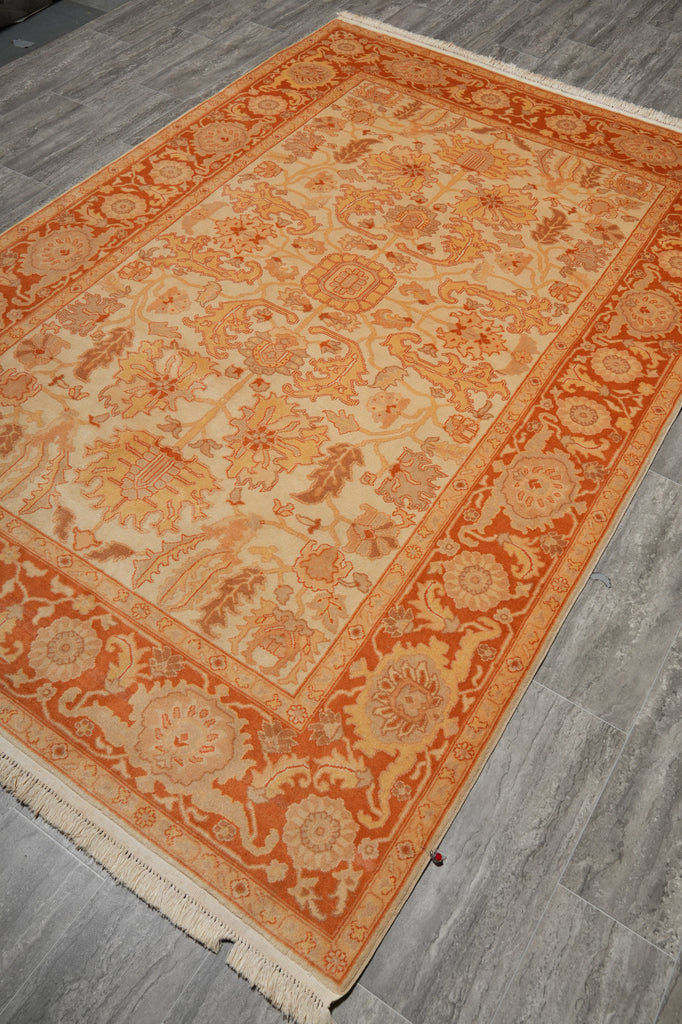 An oriental-style area rug with a warm orange and beige floral pattern, laid out on a gray wood-look floor.