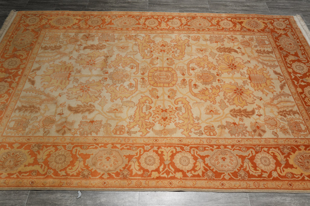 An area rug with an ornate traditional floral pattern in orange and beige tones, laid out on a dark gray tiled floor.