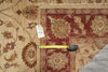Load image into Gallery viewer, A close-up of a patterned area rug with a beige and rust red floral design, showing a folded corner, fringe edge, and a yellow tape measure placed across the rug for scale.