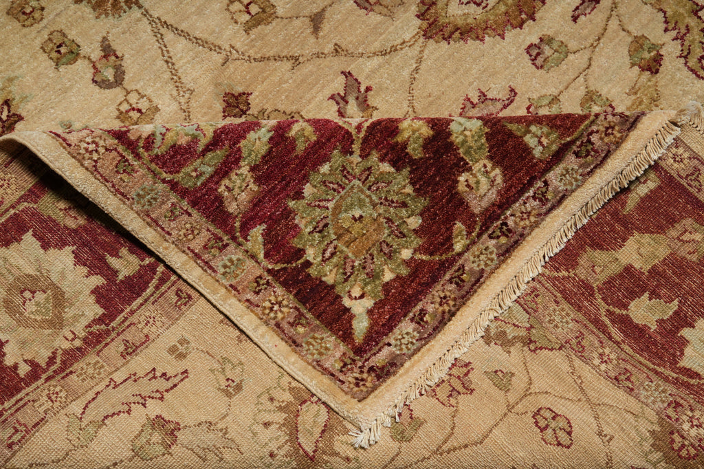 A close-up of a folded area rug showing its intricate traditional pattern in burgundy red, beige, and muted green tones.