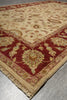 Load image into Gallery viewer, A traditional oriental-style area rug with a beige field and deep red borders, featuring floral motifs and fringed edges, laid out on a gray tiled floor.