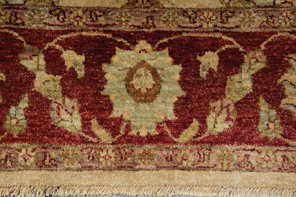Close-up of an ornate patterned rug with a deep red field, cream and beige floral motifs, and a fringed edge.