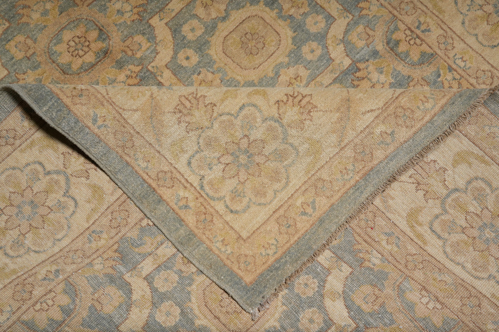 A close-up of a folded area rug showing its intricate traditional pattern in muted beige, dusty blue, and gray tones.