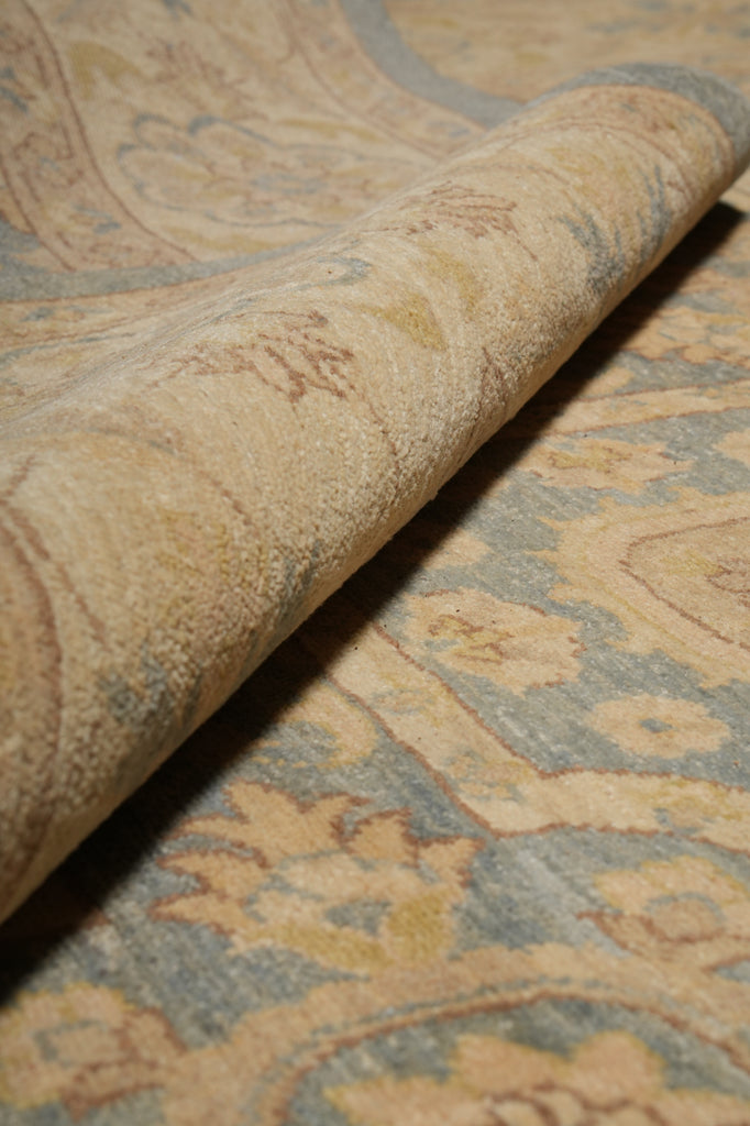 A close-up of a rolled area rug showing its plush pile and traditional floral pattern in beige, light blue, and muted yellow tones.