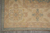 Load image into Gallery viewer, Close-up of an area rug corner showing a beige and tan field with blue and muted green floral medallions, a patterned border, and fringed edge over gray flooring.