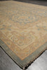 Load image into Gallery viewer, A close-up view of an area rug corner on a gray wood floor, showing a traditional floral pattern in beige, muted blue, and tan with fringed edges.