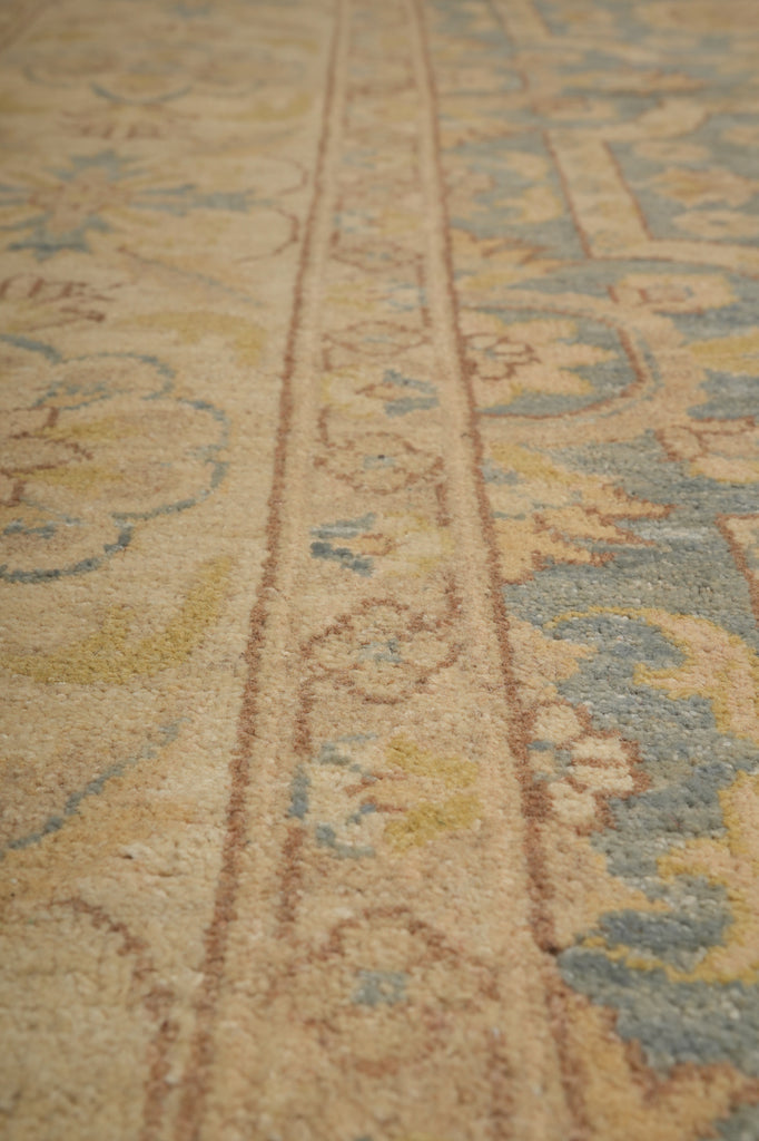 Close-up of a traditional patterned area rug with a beige base and blue, yellow, and brown ornamental motifs.