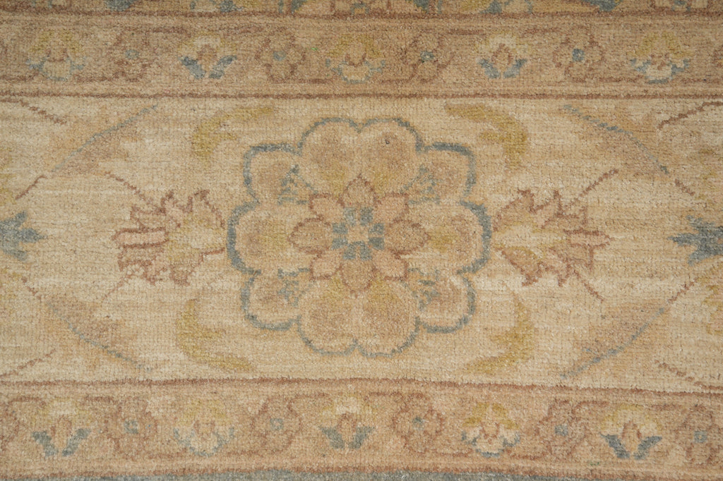 A close-up of a traditional area rug featuring a central floral medallion in muted beige, tan, dusty blue, and ochre yellow tones.