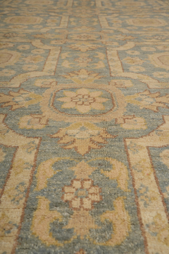 A close-up view of a traditional patterned area rug with a muted blue-gray and beige design.