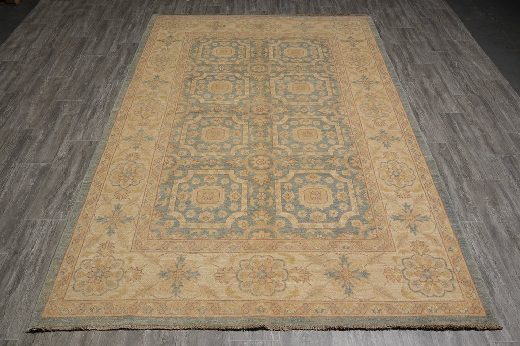 A rectangular area rug with a traditional medallion pattern in beige, muted blue, and tan, laid out on a gray wood-plank floor.
