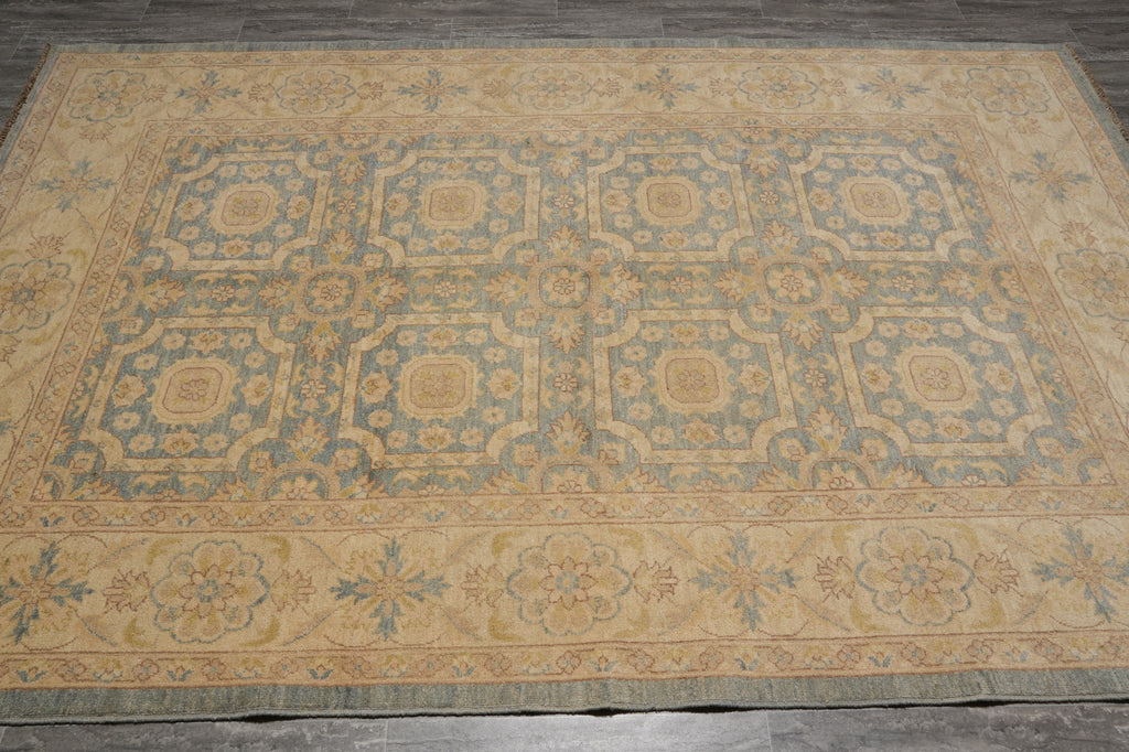 A large rectangular area rug with an ornate traditional pattern in muted blue and beige tones, laid flat on a dark gray tiled floor.