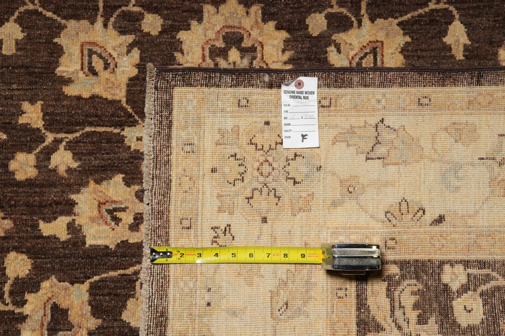A close-up of a beige patterned area rug laid over a darker brown floral rug, with a yellow tape measure and a white product tag placed on top for scale.