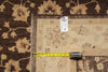 Load image into Gallery viewer, A close-up of a beige patterned area rug laid over a darker brown floral rug, with a yellow tape measure and a white product tag placed on top for scale.
