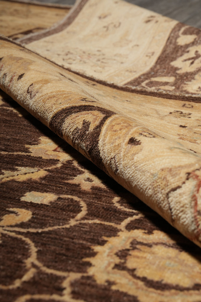 A close-up of a patterned area rug with a rolled section showing the pile and design details in beige, brown, and cream tones.