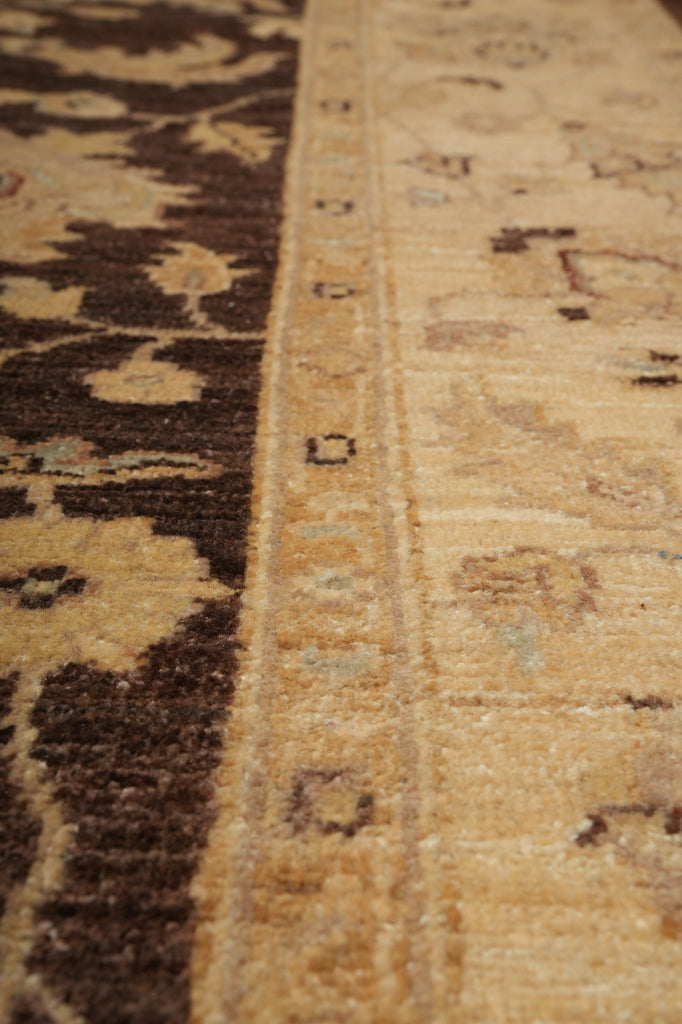 Close-up of a traditional patterned area rug showing a beige and brown border with floral motifs and a central field in warm tan tones.