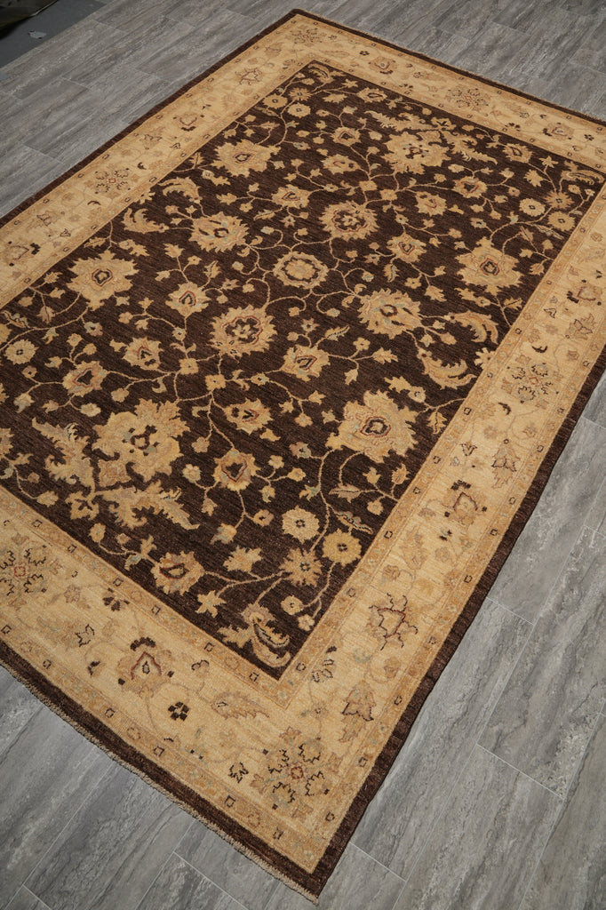 A rectangular area rug with a dark brown floral field and beige borders, shown laid out on a gray wood-look floor.