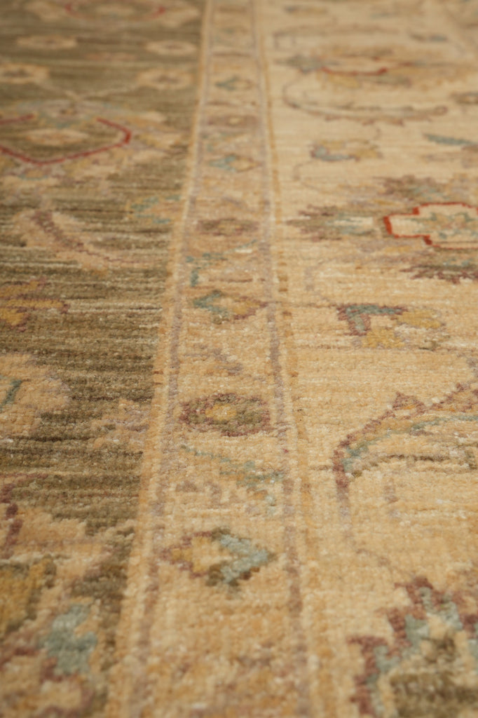 Close-up of a traditional patterned area rug with a central border and floral motifs in beige, brown, muted green, and soft red tones.
