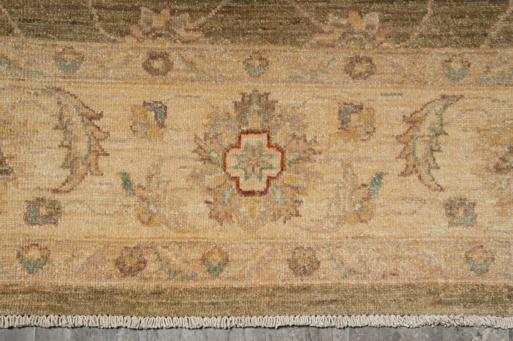A close-up of a traditional patterned rug with a beige and brown base, featuring a central medallion, floral motifs, and cream fringe at the bottom.