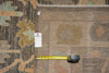 Load image into Gallery viewer, A close-up of a patterned area rug with a tape measure and a small white tag placed on it for scale, showing the rug's texture and color pattern.