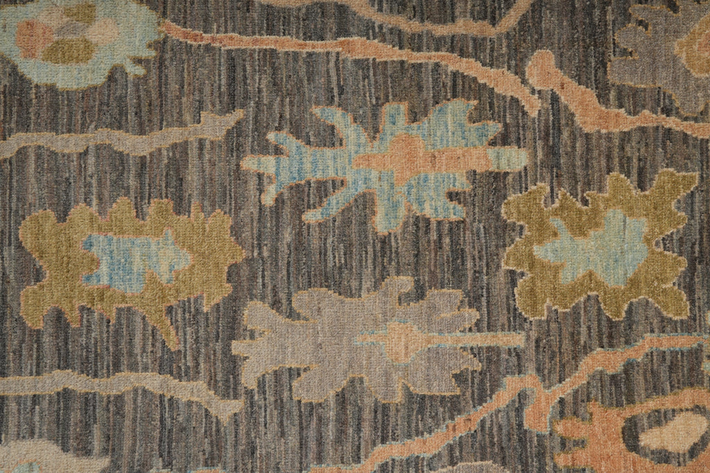 A close-up of a textured area rug featuring a vertical striped base in charcoal gray and brown, decorated with abstract floral motifs in muted blue, tan, and peach.