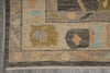 Load image into Gallery viewer, A close-up of a patterned area rug corner showing a beige base with geometric and floral motifs in muted blue, olive green, orange, and dark gray, laid over a gray floor.