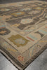 Load image into Gallery viewer, A close-up view of a traditional area rug with a geometric and floral pattern in beige, brown, muted blue, and olive green, shown on a gray concrete floor.