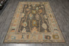Load image into Gallery viewer, A rectangular area rug with an intricate traditional pattern, displayed on a dark gray wood-look floor. The rug features a dark charcoal center with beige, light blue, and ochre accents, surrounded by a wide beige border.