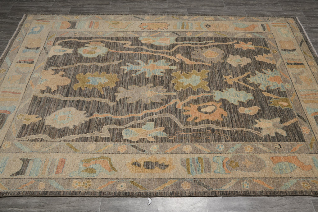 A rectangular area rug with a distressed tribal pattern in shades of brown, beige, and muted blue, laid out on a dark gray tiled floor.