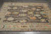Load image into Gallery viewer, A rectangular area rug with a distressed tribal pattern in shades of brown, beige, and muted blue, laid out on a dark gray tiled floor.