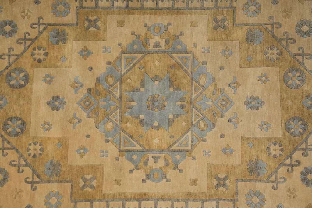 A close-up of a traditional oriental-style rug featuring a central medallion and geometric border patterns in beige, tan, muted blue, and gray.