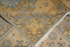 Load image into Gallery viewer, Close-up of a patterned area rug showing a folded corner that reveals the cream fringe and detailed geometric motifs in tan, beige, and muted blue-gray.