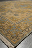 Load image into Gallery viewer, A close-up view of a traditional area rug with a beige and gray geometric pattern, featuring a fringed edge and laid out on a gray floor.