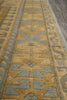 Load image into Gallery viewer, A close-up view of a patterned area rug with a warm tan and beige base, featuring geometric motifs in muted gray and a border in a taupe-brown tone.