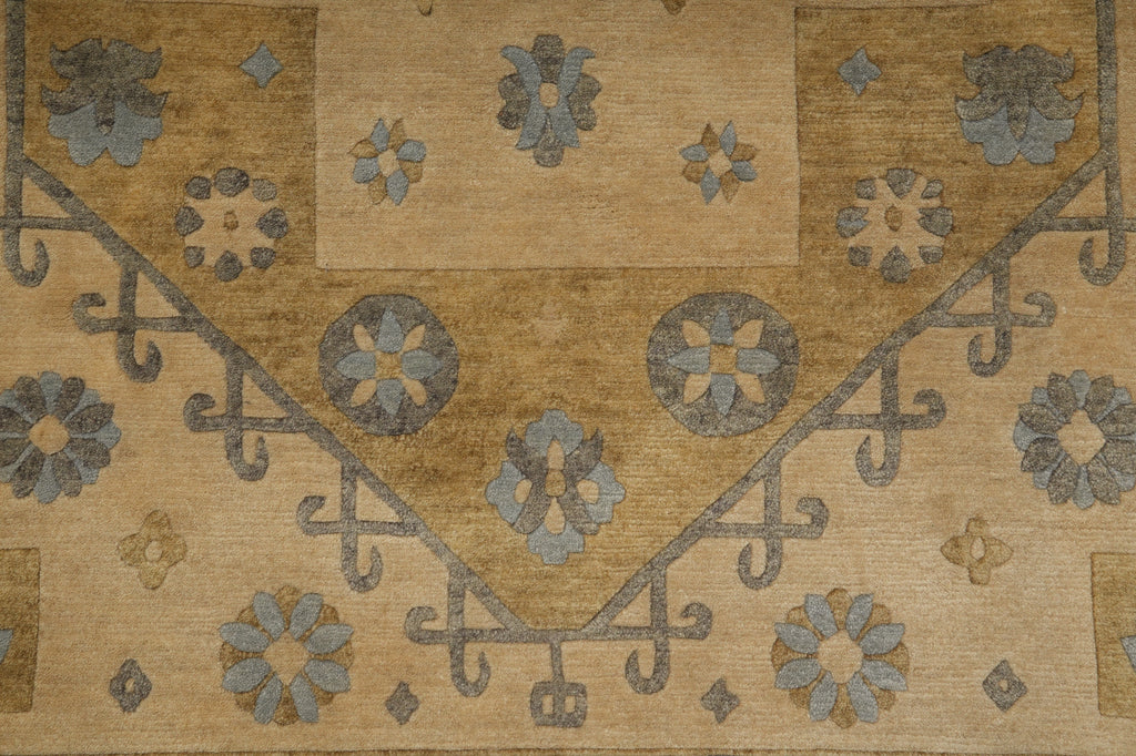 A close-up of a vintage-style patterned rug with a warm tan and beige background, featuring muted blue-gray floral medallions and scrollwork.
