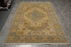 Load image into Gallery viewer, A rectangular area rug with a traditional medallion pattern in beige, gold, and muted blue, laid out on a gray wood-plank floor.