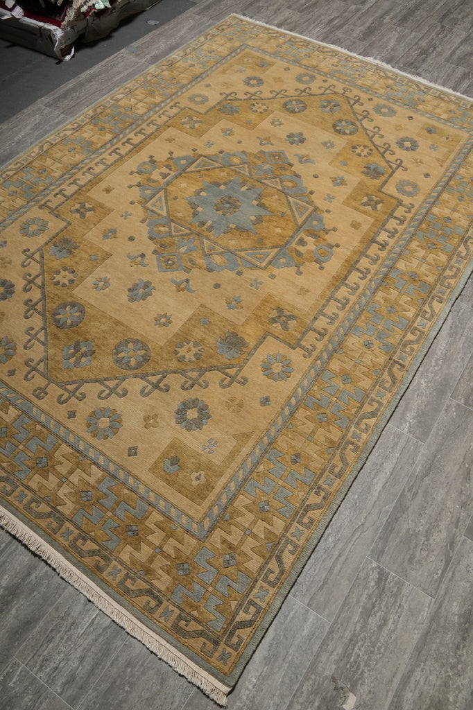 A rectangular area rug with a traditional medallion pattern in beige, brown, and muted blue-gray, shown laid out on a gray wood-look floor.