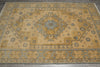 Load image into Gallery viewer, A rectangular area rug with a traditional medallion pattern in warm beige, muted gold, and dusty blue-gray, shown from a top-down perspective on a dark gray floor.