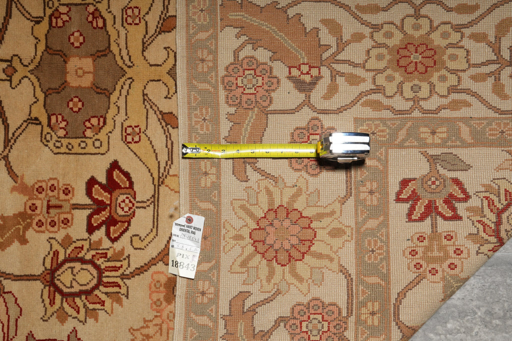An area rug with a traditional floral pattern in beige, brown, and red, shown with a yellow tape measure and a product tag.