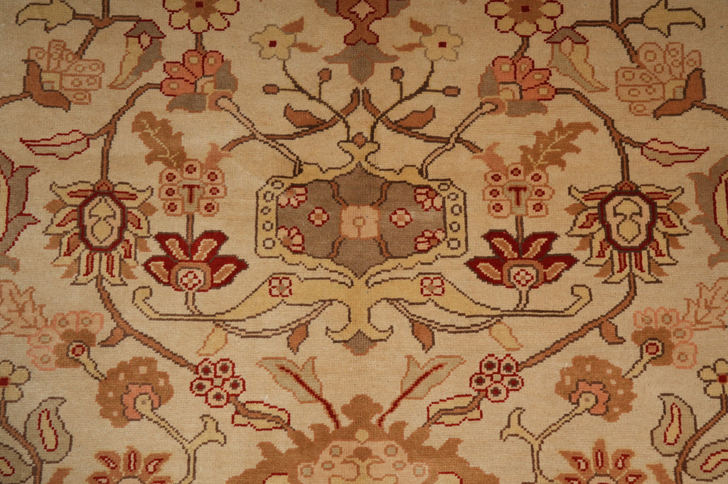 A close-up of a traditional floral patterned rug with a central medallion and scrolling vine motifs in beige, rust red, and brown tones.