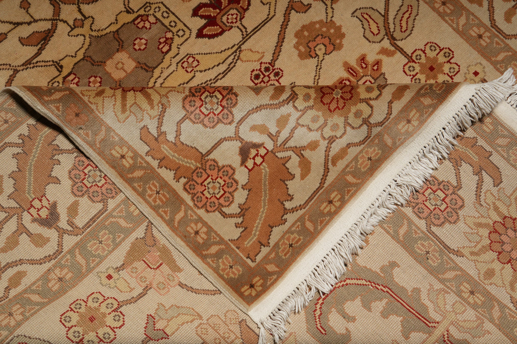 A close-up of a folded area rug with a traditional floral pattern in beige, brown, and muted red tones, featuring white fringe on one edge.