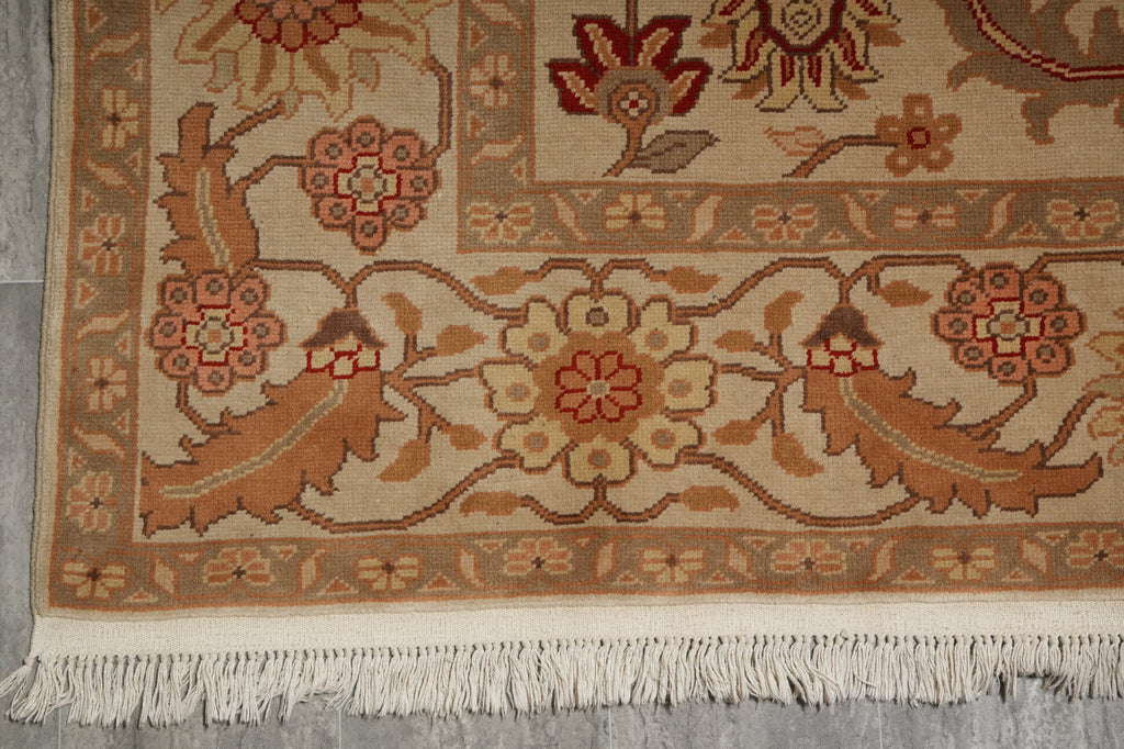 Close-up of a traditional patterned rug corner showing floral motifs, a beige and brown field, and white fringe along the bottom edge.