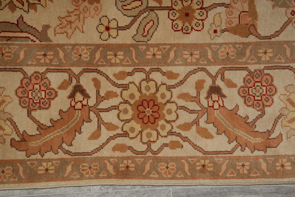 A close-up of a traditional patterned rug featuring a central floral motif, stylized birds, and geometric borders in beige, brown, and muted red tones.