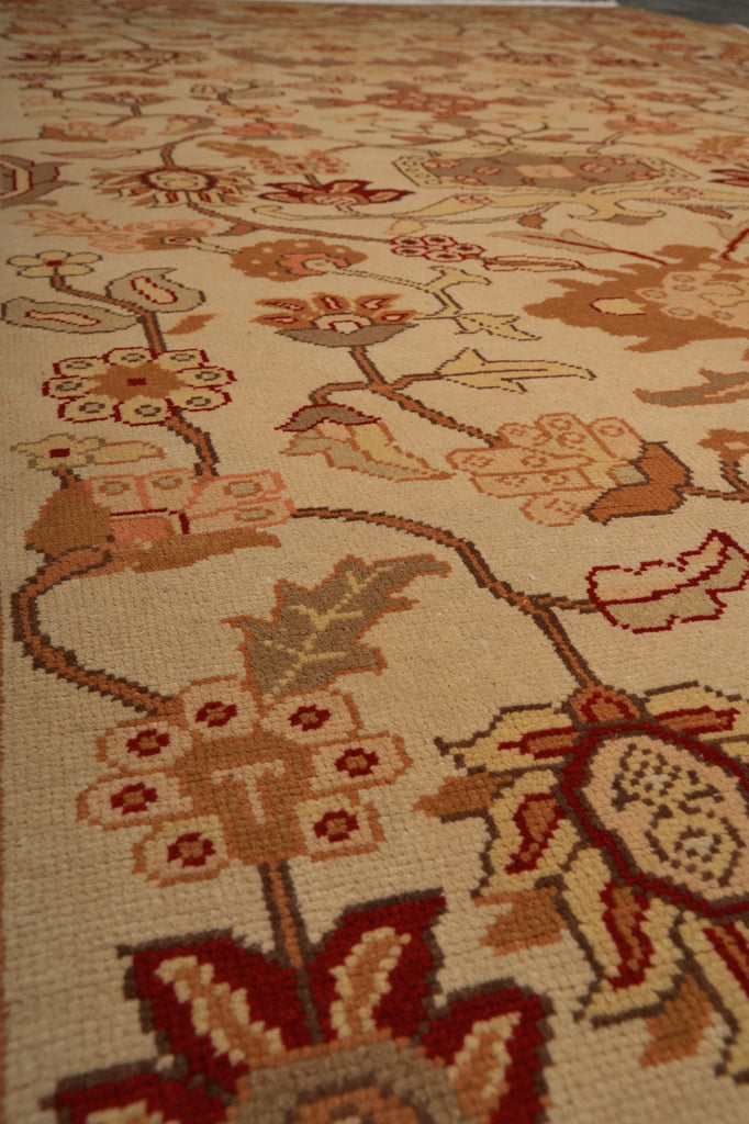 Close-up of a woven area rug with a vintage floral pattern in beige, rust red, brown, and muted green tones.
