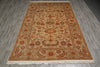 Load image into Gallery viewer, A rectangular area rug with an intricate traditional floral and vine pattern, laid flat on a gray wood-look floor. The rug features a warm beige center, a golden-brown border, and cream fringe at the bottom.