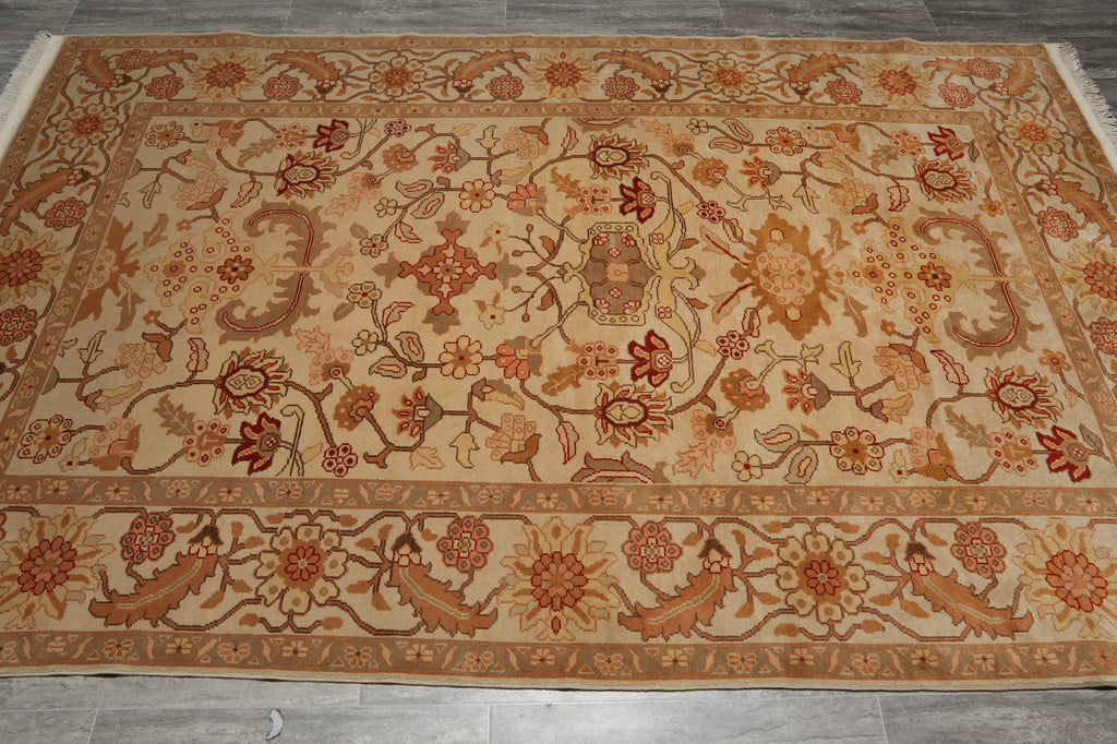 A rectangular area rug with an intricate floral and botanical pattern in warm beige, rust red, and brown tones, laid flat on a gray tiled floor.