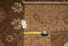 Load image into Gallery viewer, A close-up of a patterned area rug with a yellow tape measure and a white tag placed on it for scale, showing the rug's intricate floral and geometric designs in brown, beige, and rust tones.