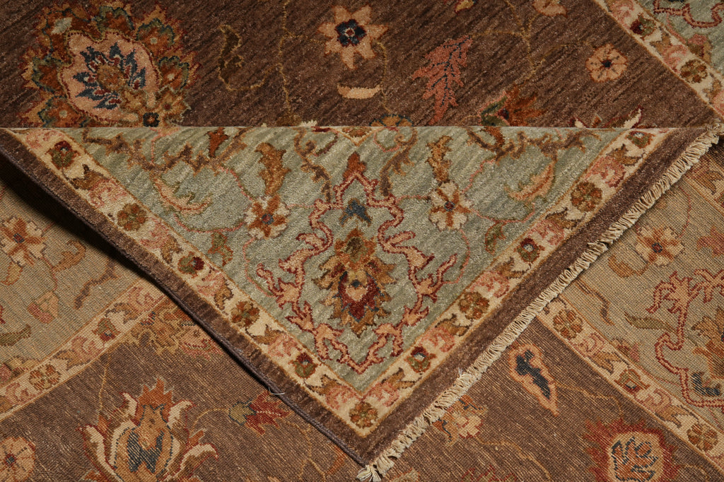 A close-up of a traditional patterned rug with a folded corner revealing a dusty blue-green central field and ornate floral motifs in brown, beige, rust, and cream.