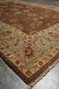 Load image into Gallery viewer, A traditional oriental area rug with a brown central field, a beige and rust border, and a light sage green corner panel, shown on a gray tiled floor.