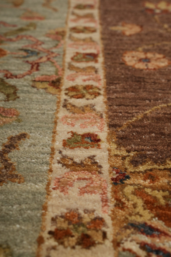 Close-up of a patterned area rug showing a central cream border with floral motifs and adjacent sections in muted green and brown tones.