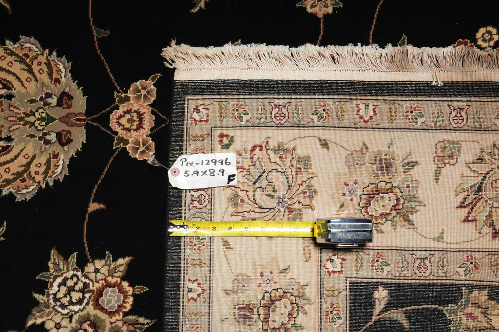 A close-up of a patterned area rug with cream fringe, shown alongside a yellow tape measure and a small white tag with product code 'Doc-12946 5.9x8.